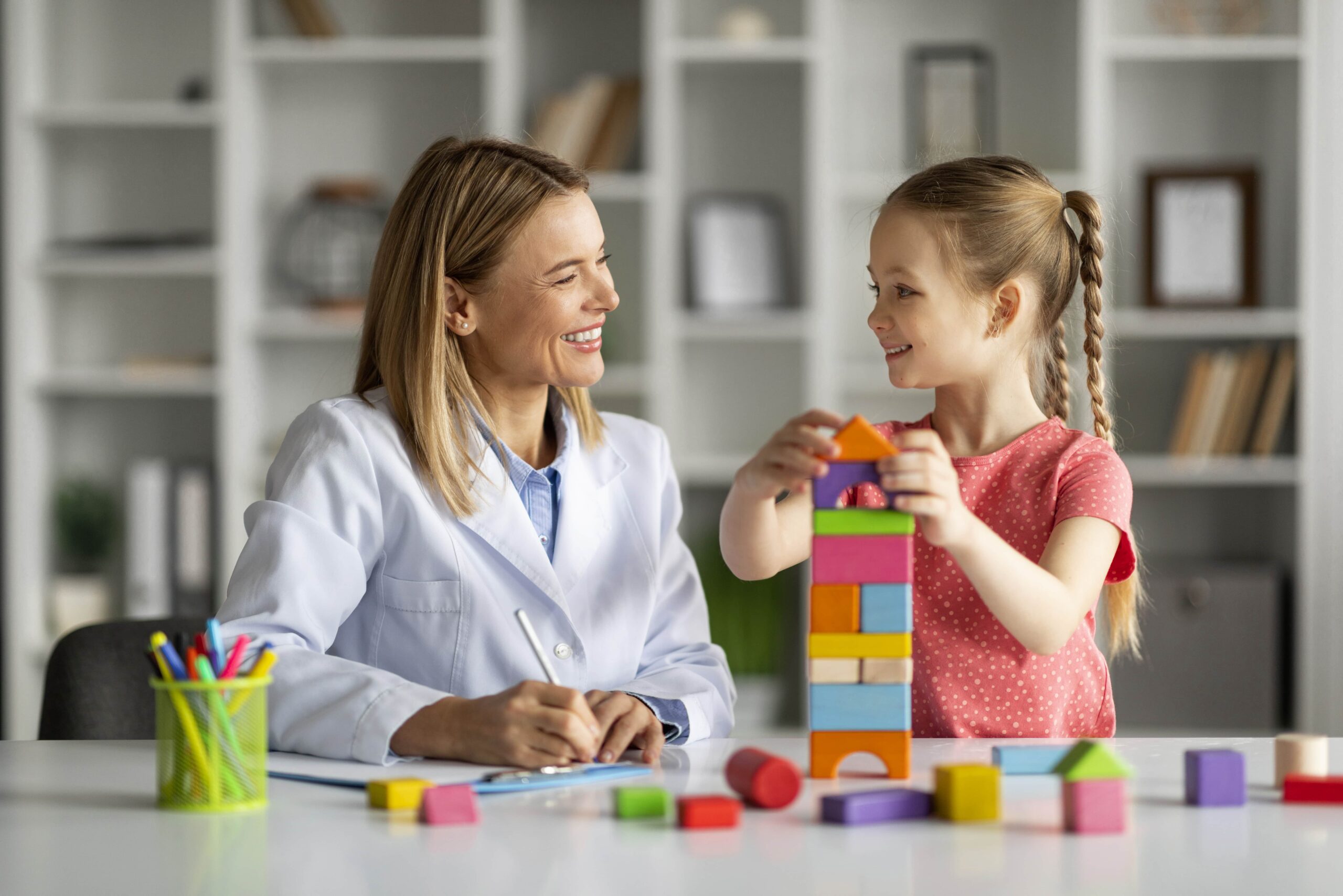 cute-little-girl-child-development-specialist-lady-playing-with-colorful-bricks-min
