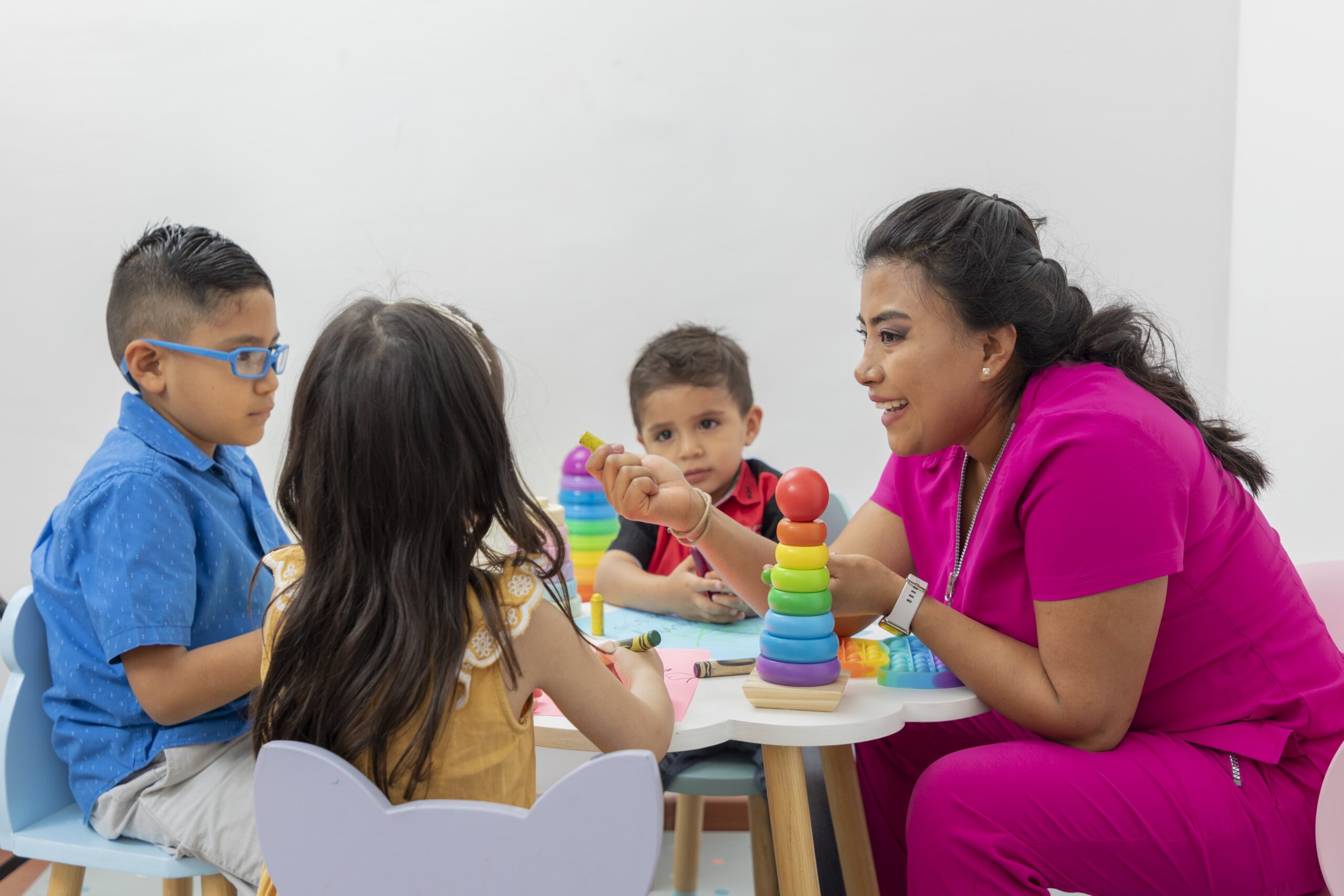 female-pediatrician-sitting-table-with-several-children-playing-her-medical-office-min